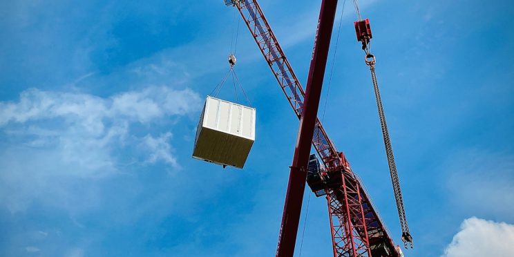 Crane picking up a large container with a blue sky behind it